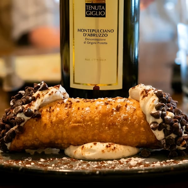 Chocolate chip cannoli with whipped cream on a plate, a Montepulciano d'Abruzzo wine bottle behind it.