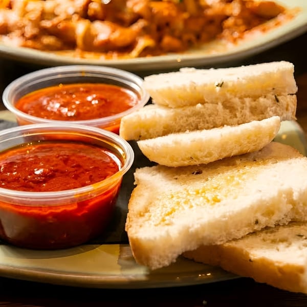 Slices of garlic bread and two cups of red dipping sauce on a green plate.