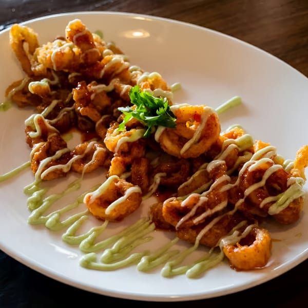 Crispy fried calamari with sweet chili and creamy green drizzles, garnished with cilantro.