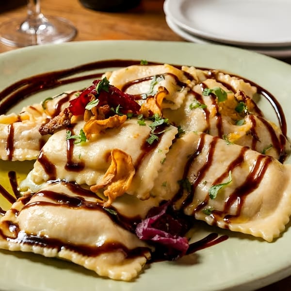 Ravioli pasta dish with dark sauce, herbs, mushrooms, and red onion on a light green plate.